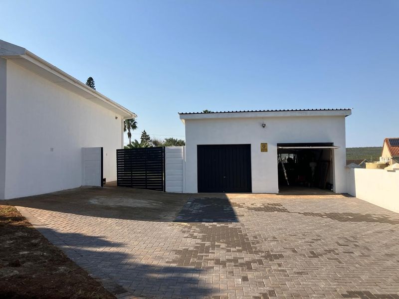 Exterior view of a detached garage with a paved driveway, secure gate, and white rendered walls.