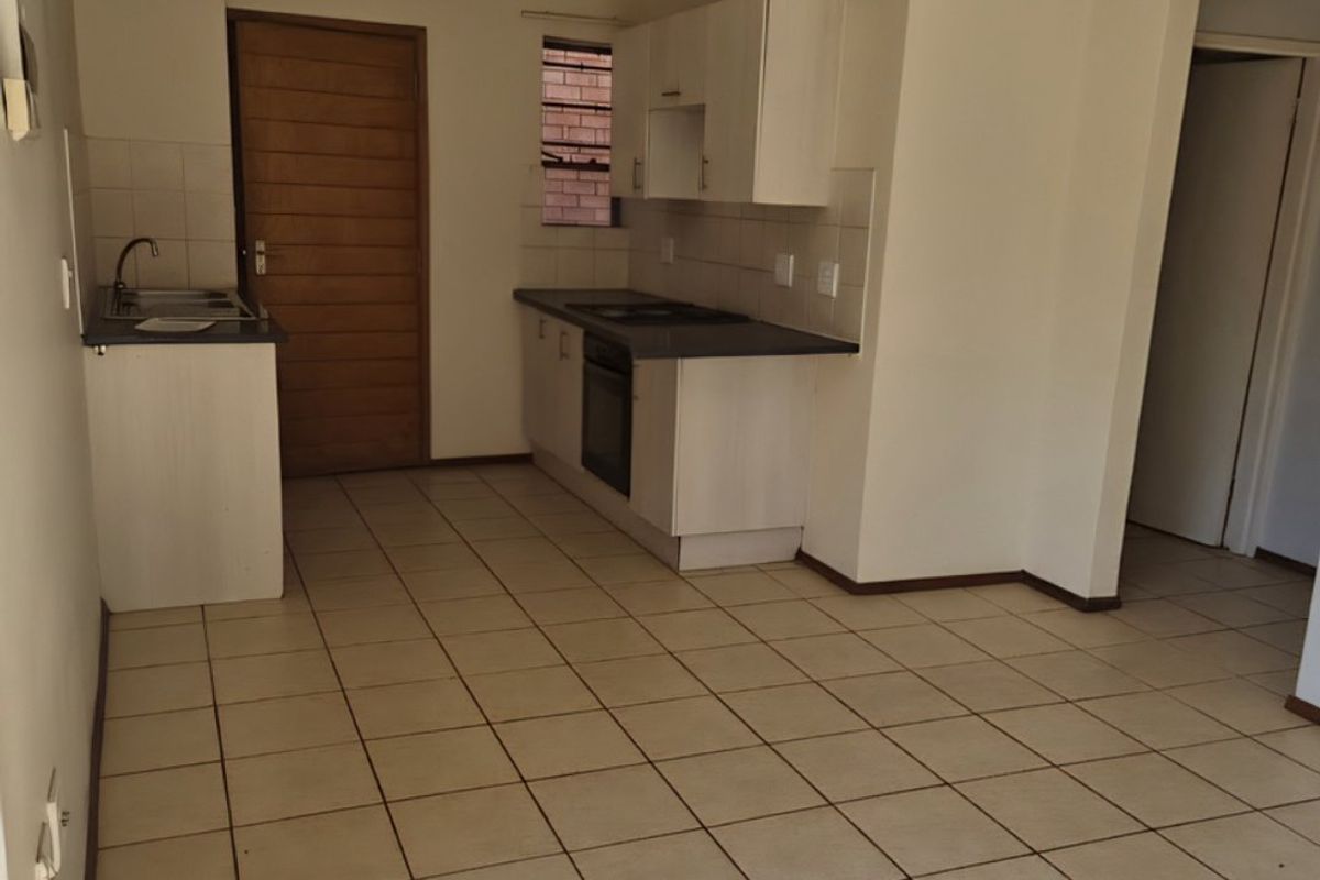 An empty kitchen featuring built-in cabinetry, a built-in oven, hob, and ceramic tiled flooring, offering a functional space ready for personalization.