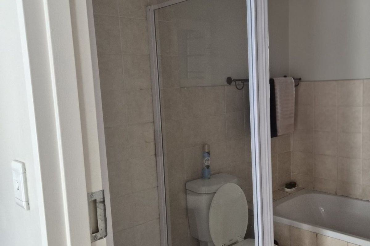 A functional bathroom featuring a separate shower enclosure, a standard toilet, and a built-in bathtub with neutral wall and floor tiling.