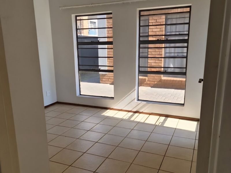 An empty bedroom featuring neutral tiled flooring and large windows fitted with security bars, offering a bright and functional space.