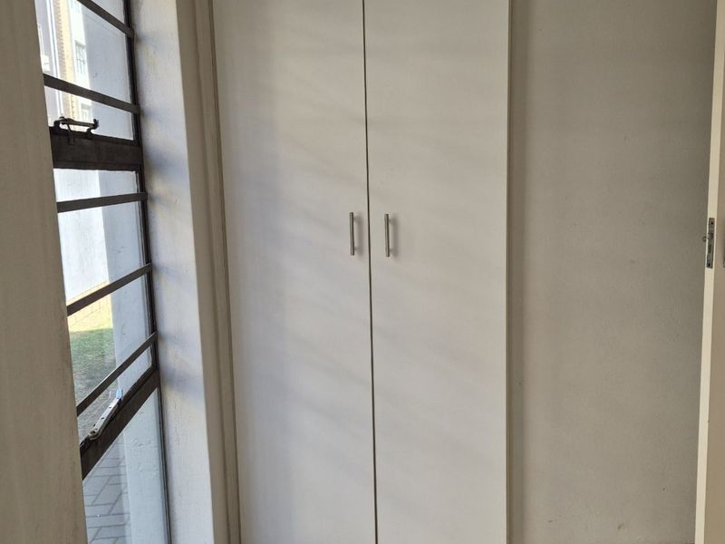 A simple bedroom featuring tiled flooring, a built-in cupboard, and a window with security bars.