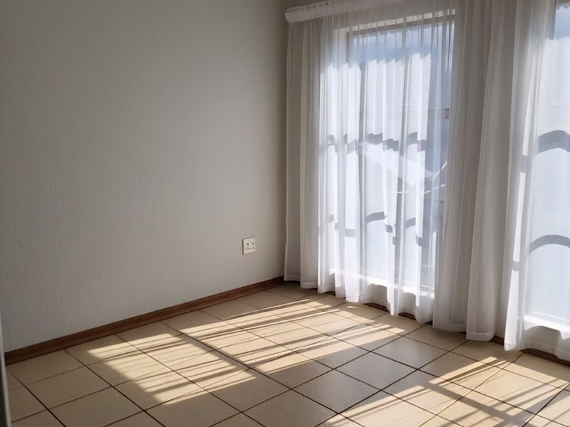 A bright, empty bedroom featuring neutral tiled flooring and large windows with sheer curtains, offering a clean and versatile space.