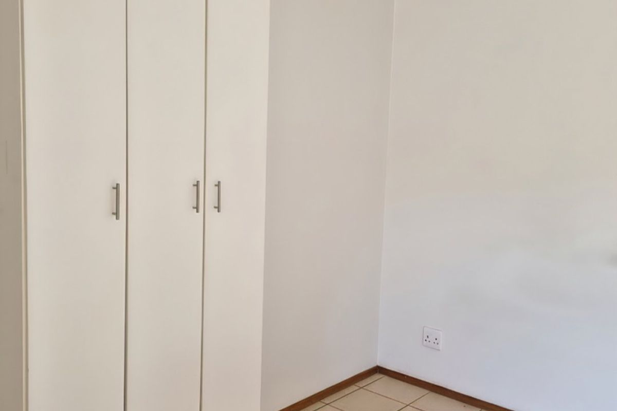 A clean, empty bedroom featuring neutral tiled flooring and a white built-in wardrobe with modern handles.