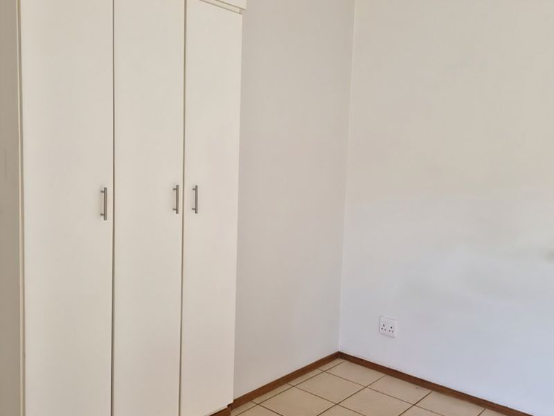 A clean, empty bedroom featuring neutral tiled flooring and a white built-in wardrobe with modern handles.