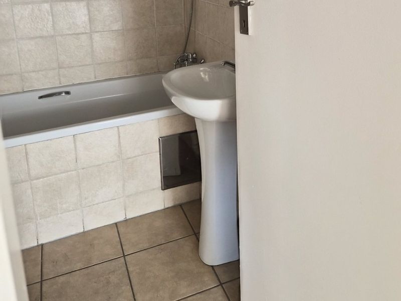 A compact bathroom featuring a pedestal basin, a bathtub with a handheld shower attachment, and neutral tiled finishes.
