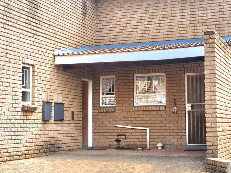 Front exterior view of the apartment featuring a brick facade, paved driveway, security gates, and external utility access points.