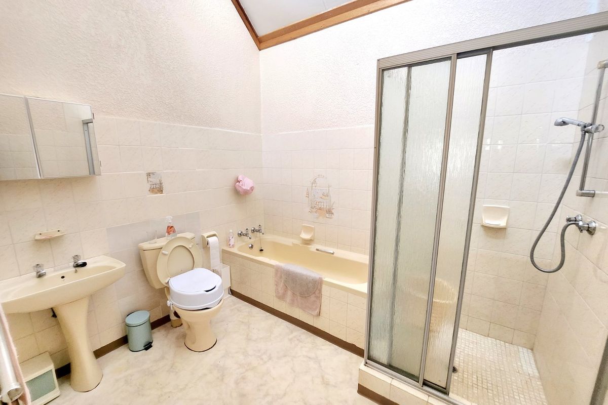 A spacious bathroom featuring a pedestal basin, toilet, built-in bathtub, and a separate shower enclosure with tiled walls and a vaulted ceiling.
