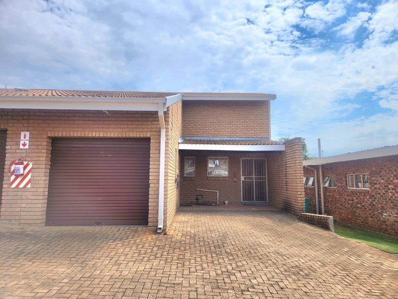 Front exterior view of the apartment featuring a brick facade, a single roller garage door, and a paved driveway entrance with security gate.