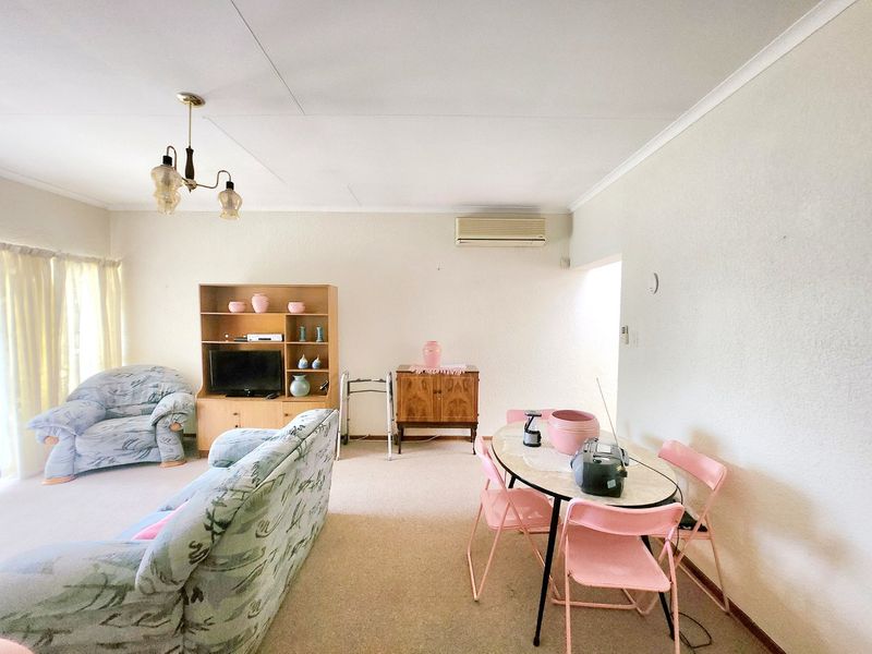 An open-plan living and dining area featuring carpeted flooring, a split-system air conditioner, and a classic chandelier, offering a functional and versatile living space.