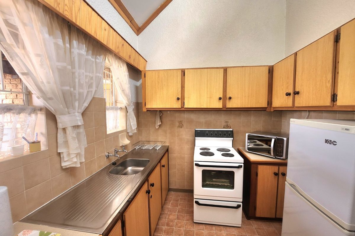 A functional kitchen featuring wooden cabinetry, a stainless steel sink, tiled splashback, and a vaulted ceiling, offering a classic, dated aesthetic.