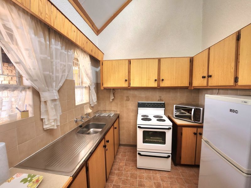 A functional kitchen featuring wooden cabinetry, a stainless steel sink, tiled splashback, and a vaulted ceiling, offering a classic, dated aesthetic.