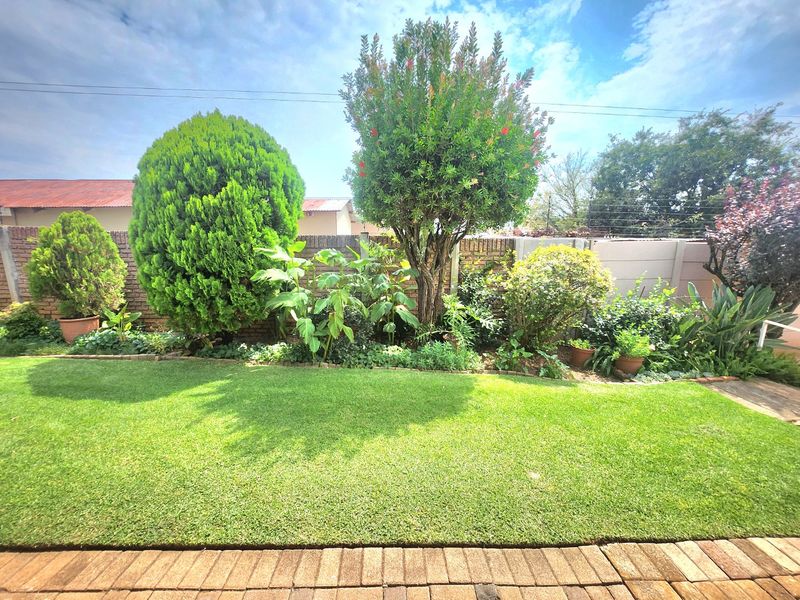 A well-maintained private garden featuring a lush green lawn, established trees, and a secure brick boundary wall.