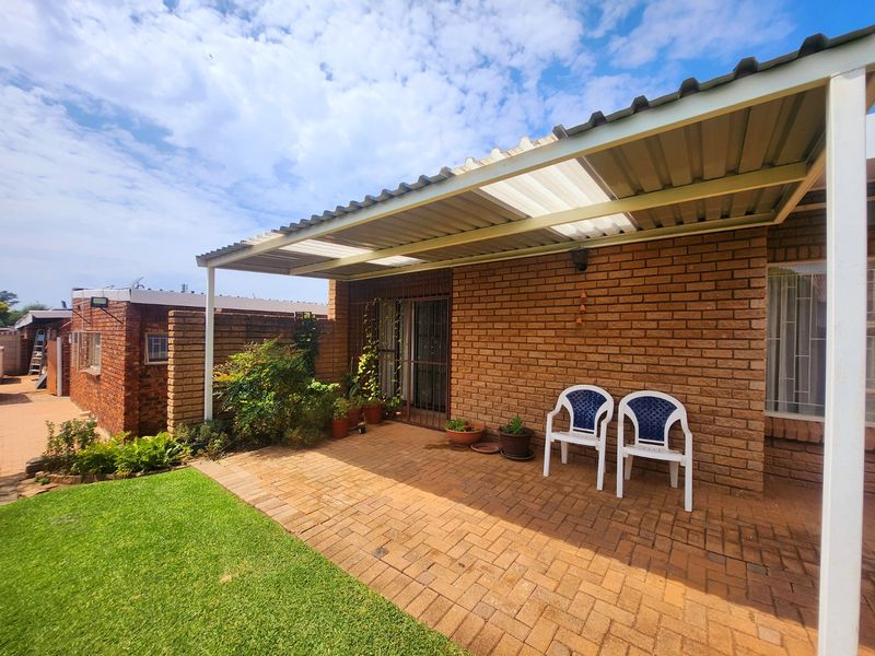 A covered brick-paved patio area featuring a corrugated roof, providing a functional outdoor space adjacent to the main building structure.