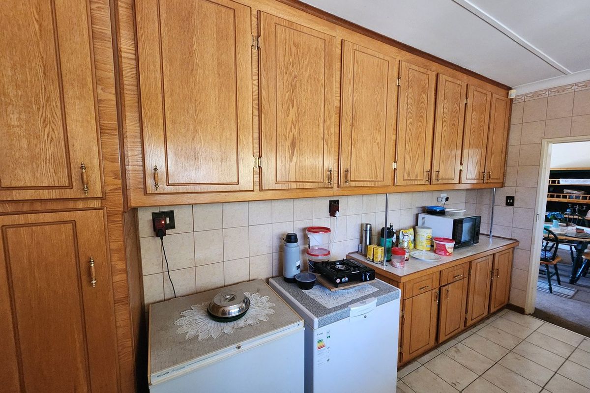 A dated kitchen featuring extensive wooden cabinetry, tiled backsplash, and tiled flooring, offering a functional layout with significant potential for modern renovation.