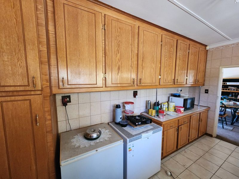 A dated kitchen featuring extensive wooden cabinetry, tiled backsplash, and tiled flooring, offering a functional layout with significant potential for modern renovation.