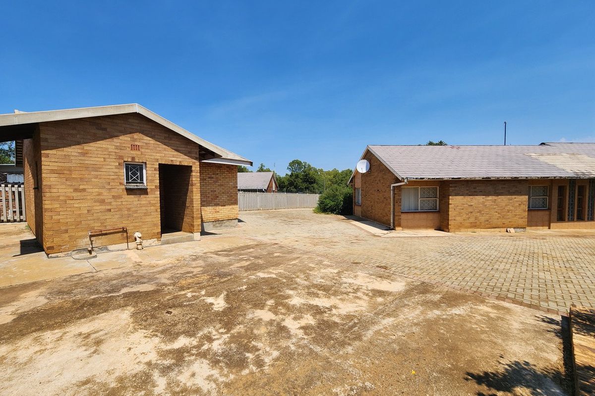 Rear exterior view of the property featuring brick buildings, paved courtyard area, and tiled roofing with visible signs of weathering.