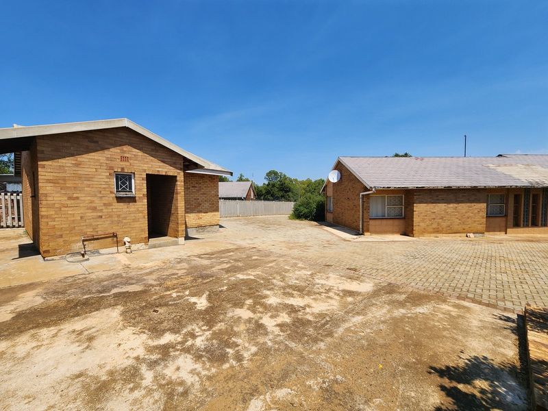 Rear exterior view of the property featuring brick buildings, paved courtyard area, and tiled roofing with visible signs of weathering.