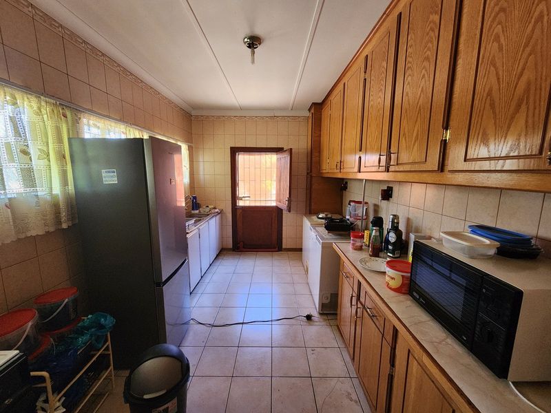 A functional kitchen featuring wooden cabinetry, tiled splashbacks, and tiled flooring, providing a practical workspace with direct access to the exterior.