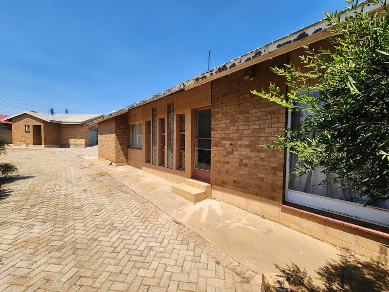 Rear exterior view of a face brick house featuring a paved driveway, glass block windows, and a concrete apron requiring maintenance on the roof fascia.