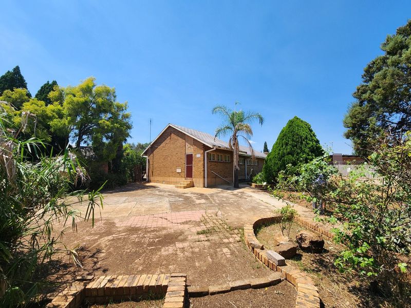 Rear view of a brick house featuring a paved patio area, established garden beds with brick edging, and a concrete driveway.