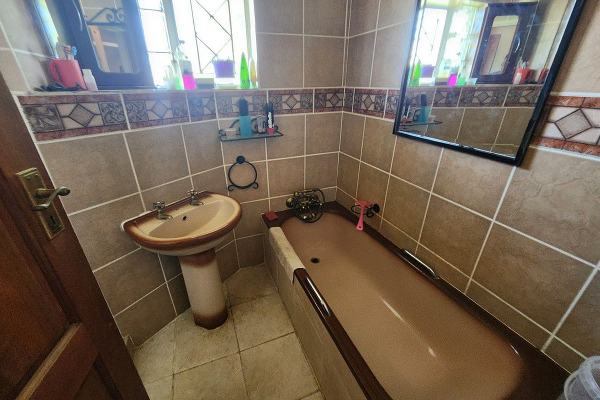 A compact bathroom featuring dated brown sanitaryware, ceramic wall and floor tiling, and a wall-mounted mirror.