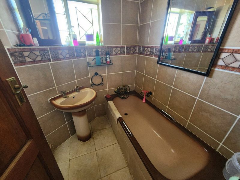 A compact bathroom featuring dated brown sanitaryware, ceramic wall and floor tiling, and a wall-mounted mirror.