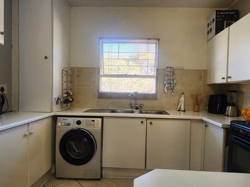 A functional kitchen featuring built-in cabinetry, tiled backsplash, and integrated sink area, offering a practical layout with potential for cosmetic modernization.