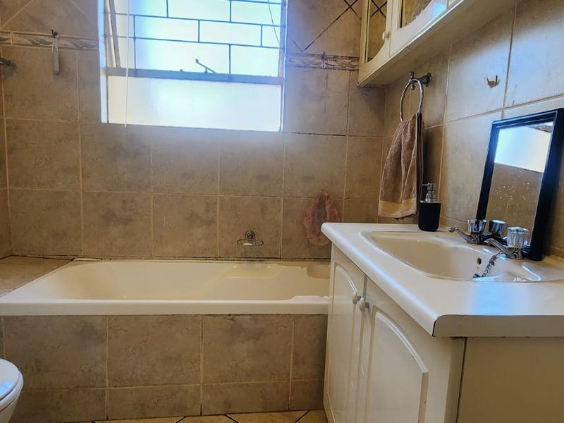 A dated bathroom featuring a built-in bathtub, vanity cabinet with basin, and toilet, finished with neutral wall and floor tiles.