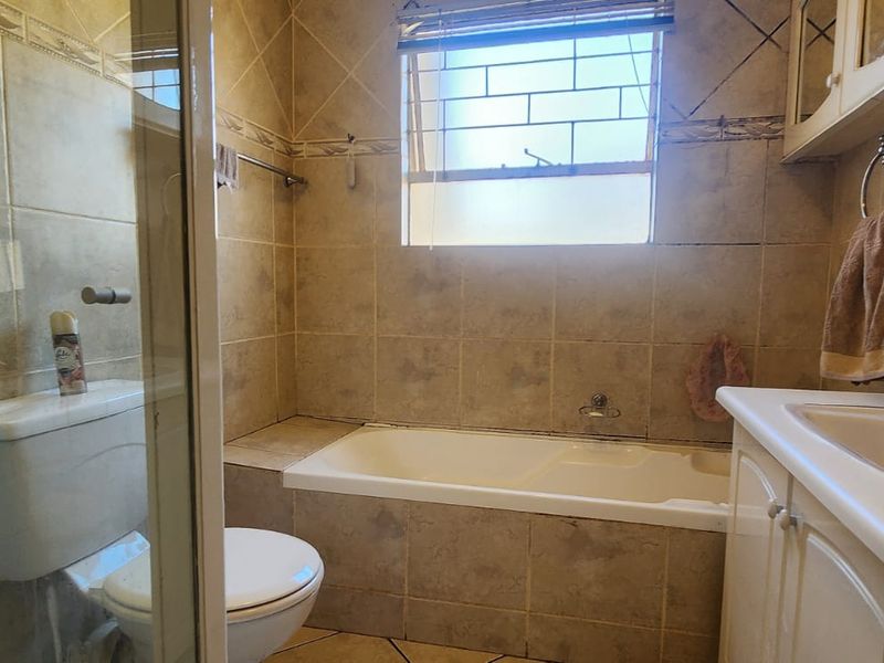 A functional bathroom featuring a built-in bathtub, separate shower enclosure, vanity cabinet with basin, and tiled finishes throughout.