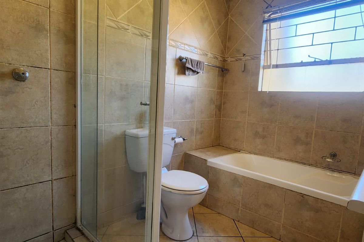 A functional bathroom featuring a shower enclosure, bathtub, toilet, and vanity basin with neutral wall and floor tiling.