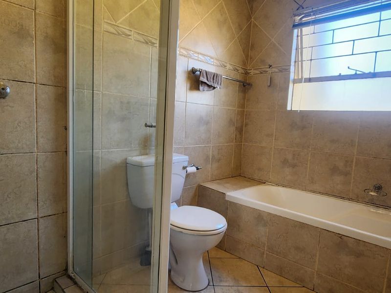 A functional bathroom featuring a shower enclosure, bathtub, toilet, and vanity basin with neutral wall and floor tiling.
