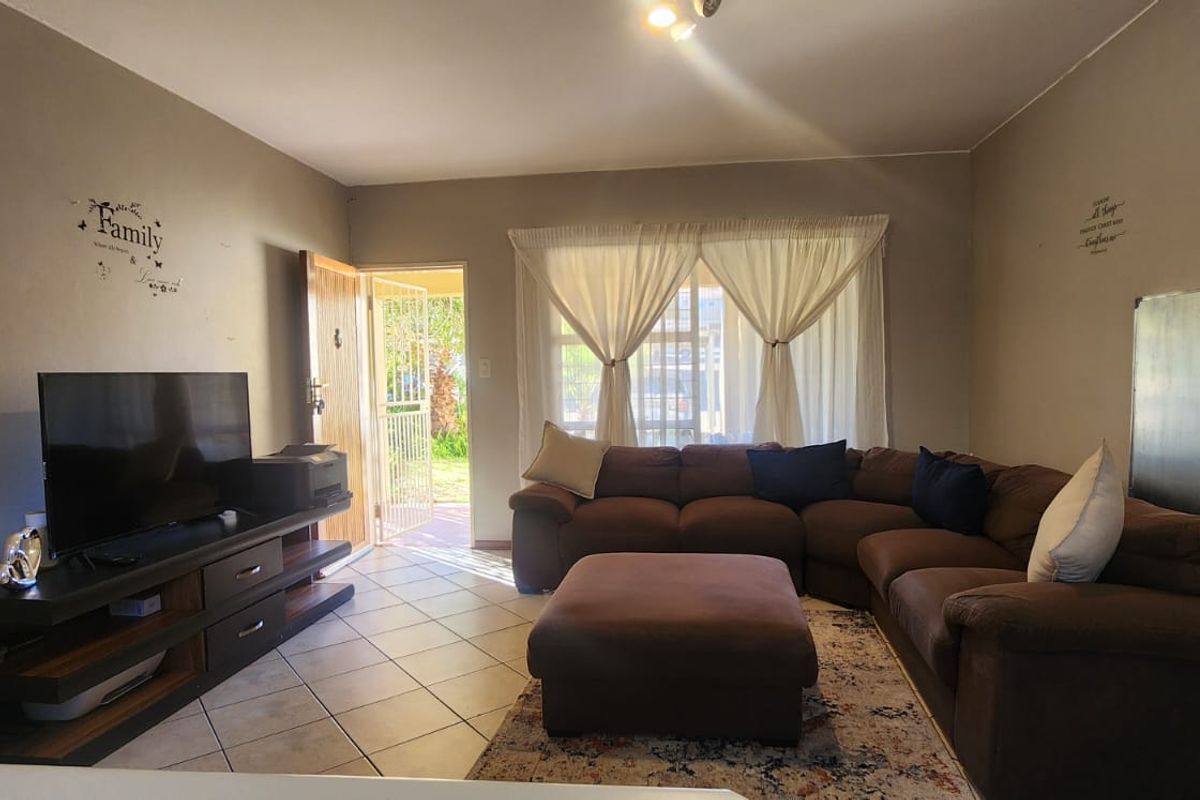 A functional living room featuring ceramic floor tiles and direct access to the exterior through a security gate and sliding door.