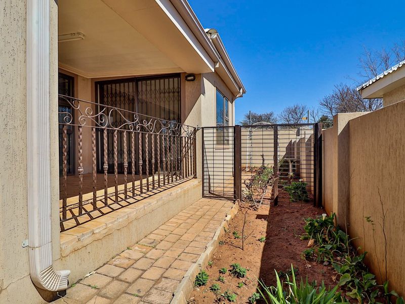 A covered patio area featuring a paved walkway, wrought iron railing, and a secure side gate leading to the garden space.