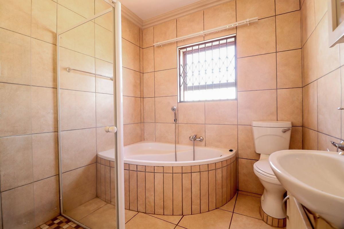 A functional bathroom featuring a corner bathtub, separate glass shower enclosure, pedestal basin, and neutral floor-to-ceiling tiling.