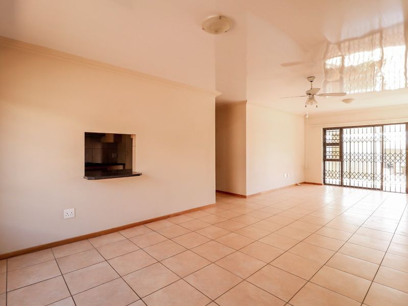 Spacious, empty living area featuring tiled flooring, a ceiling fan, and a serving hatch connecting to the kitchen, with access to a secure patio.