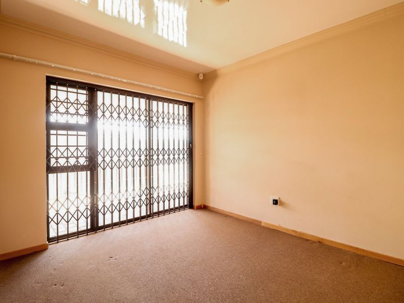 An empty bedroom featuring carpeted flooring, coved ceilings, and a sliding security gate over the window.