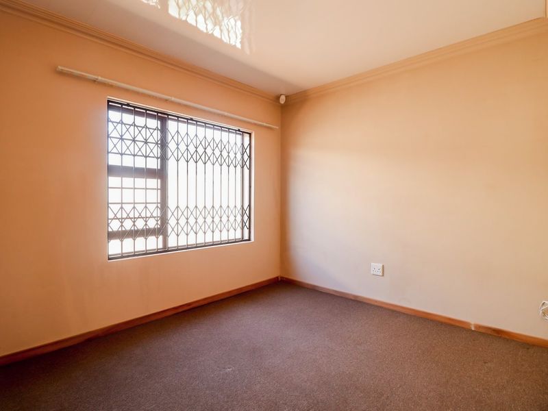 A clean, empty bedroom featuring neutral walls, carpeted flooring, and a window fitted with a security gate.