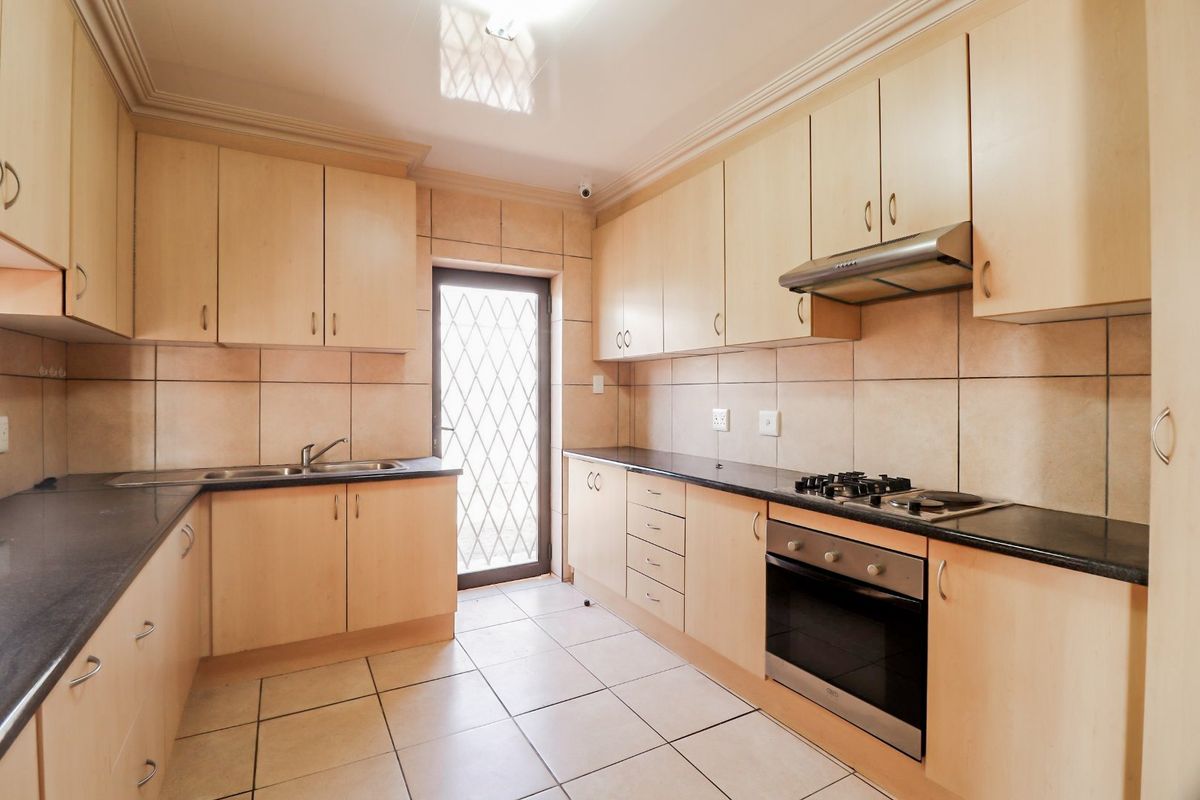 A functional kitchen featuring light wood cabinetry, dark countertops, built-in oven, gas hob, and tiled finishes with direct access to the exterior.