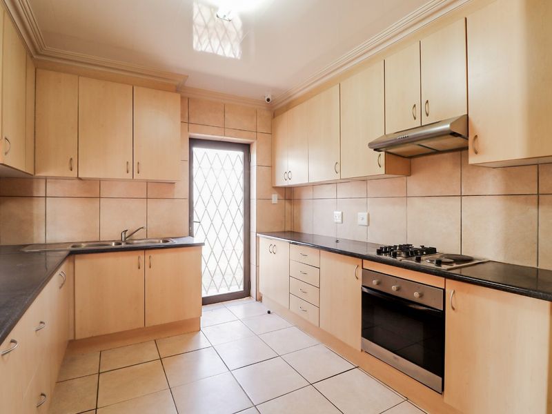 A functional kitchen featuring light wood cabinetry, dark countertops, built-in oven, gas hob, and tiled finishes with direct access to the exterior.