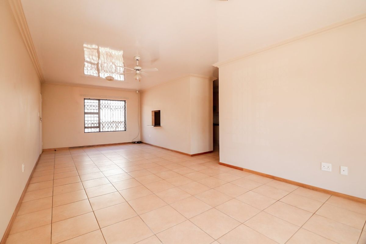 Spacious, empty living area featuring neutral tiled flooring, a ceiling fan, and a pass-through window connecting to the kitchen area.