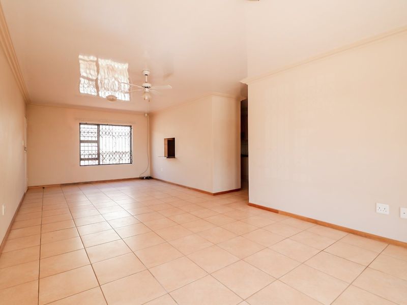 Spacious, empty living area featuring neutral tiled flooring, a ceiling fan, and a pass-through window connecting to the kitchen area.
