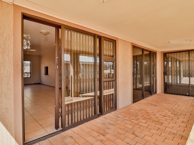 A covered patio area featuring brick paving and large sliding glass doors with security gates, providing seamless access to the interior living space.
