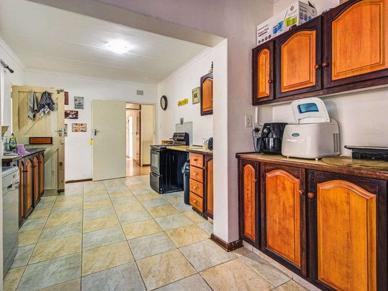 A functional kitchen featuring traditional wooden cabinetry, tiled flooring, and a freestanding stove, offering potential for a modern renovation.