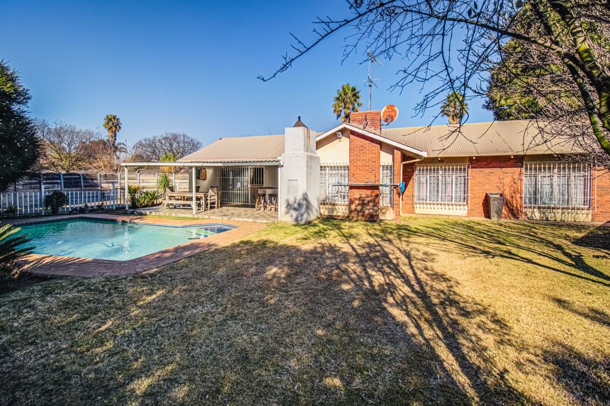 Rear view of the property featuring a swimming pool, covered patio area, and a brick facade with security bars on the windows.