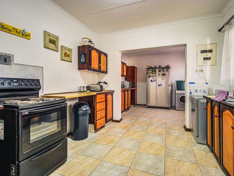 A functional kitchen featuring tiled flooring, built-in wooden cabinetry, and a freestanding stove, with an adjacent utility area for laundry appliances.