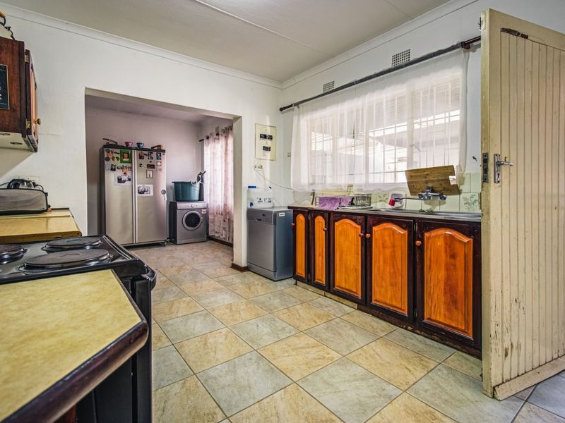 A functional kitchen featuring built-in wooden cabinetry, tiled flooring, and a double sink, with an adjacent utility area for laundry appliances.