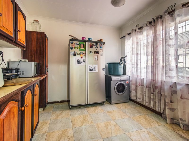 A functional laundry room featuring tiled flooring, fitted cabinetry, and a window with security bars, offering potential for modernization.