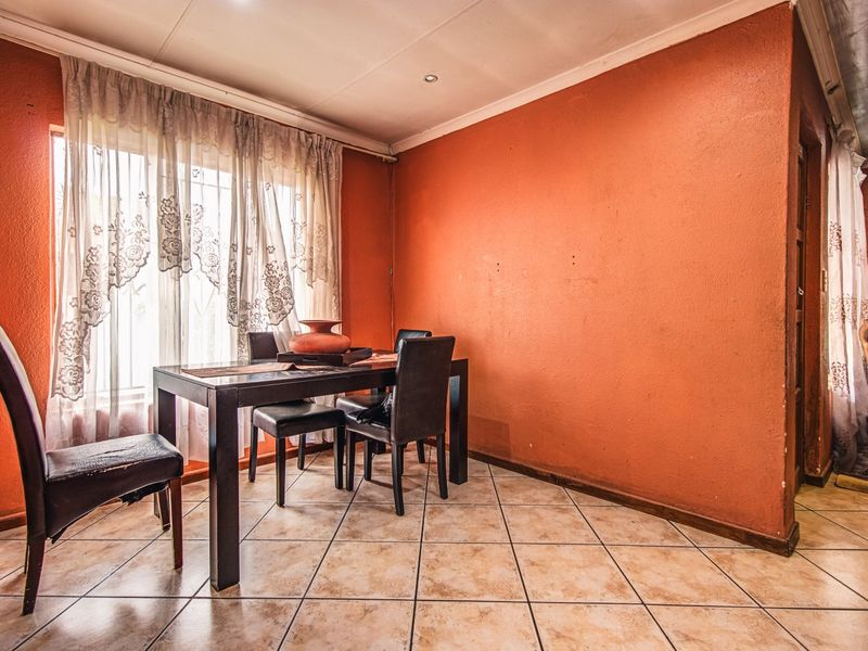A dining room featuring tiled flooring and recessed lighting, currently finished with bold orange wall paint.