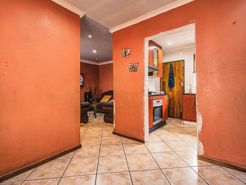 A view from the hallway looking into the kitchen and living area, featuring tiled flooring and visible wear on the wall finishes.