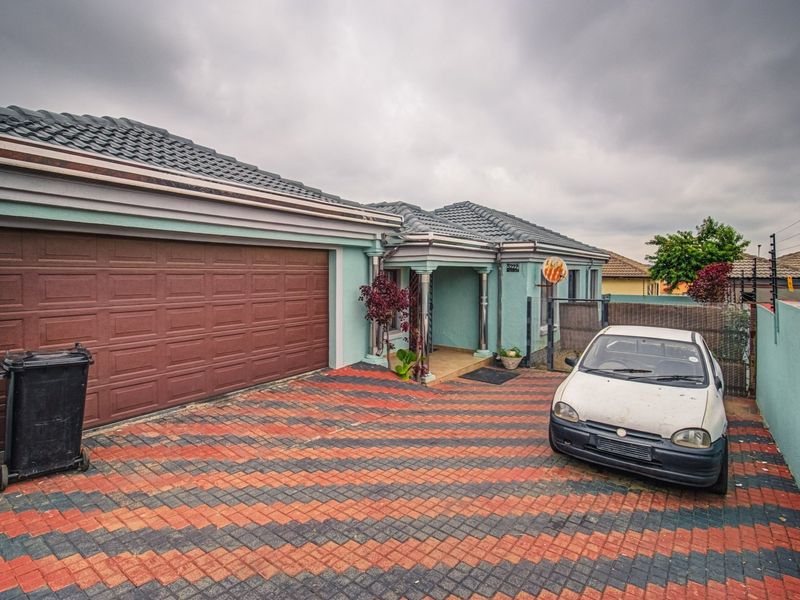 Front elevation of a residential property featuring a double garage, paved driveway, and secure boundary wall with electric fencing.
